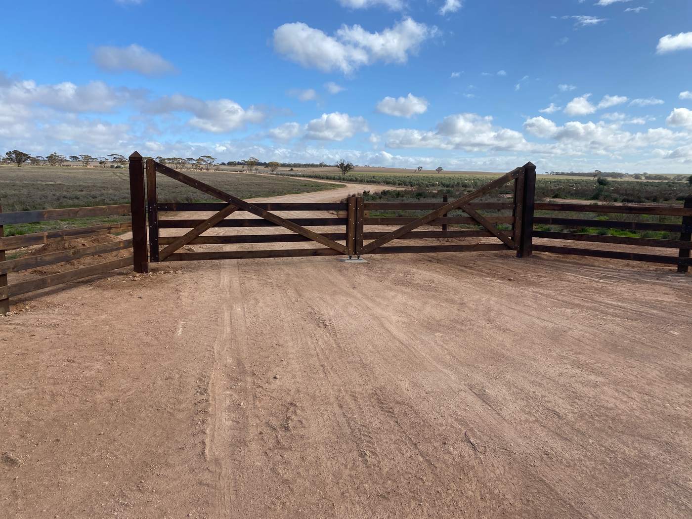 Wide timber farm entrance gates with matching rails, under a big sky